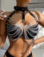 Close-up of a woman wearing a black faux leather harness bra adorned with cascading silver chains and a central O-ring detail, styled over a black bikini top.